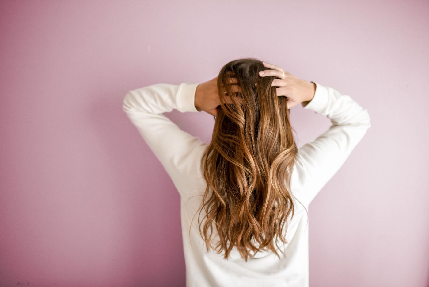 Woman running her hands through long wavy hair against a soft pink wall